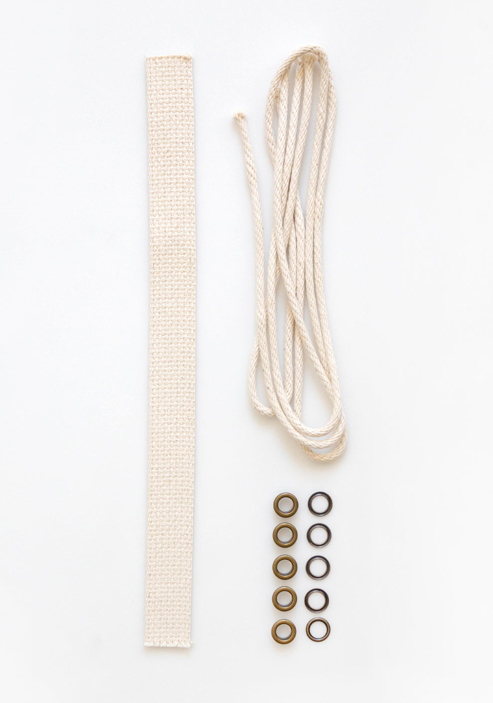 Model: Cotton Handle | Flatlay of Field Bag notions kit with cotton webbing, drawstring cord, and brass grommets on white background.