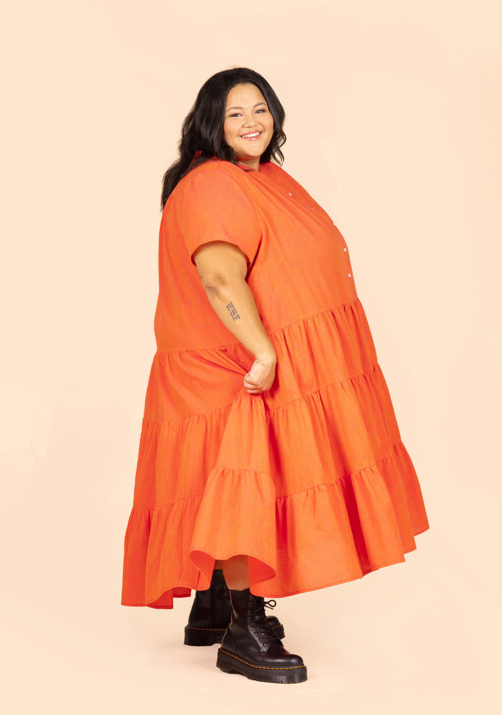 Side view of long Poppy Dress View B in orange linen as model lifts hem to show movement.