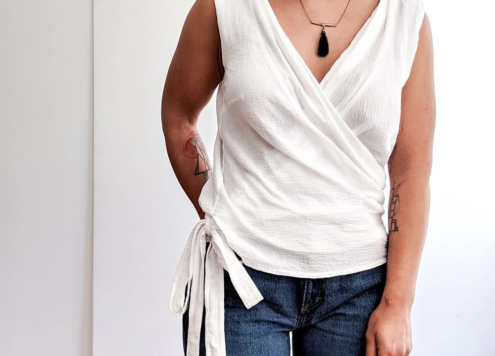 Woman wearing white linen Hadley wrap top modification with tie closure at side waist paired with dark denim jeans.
