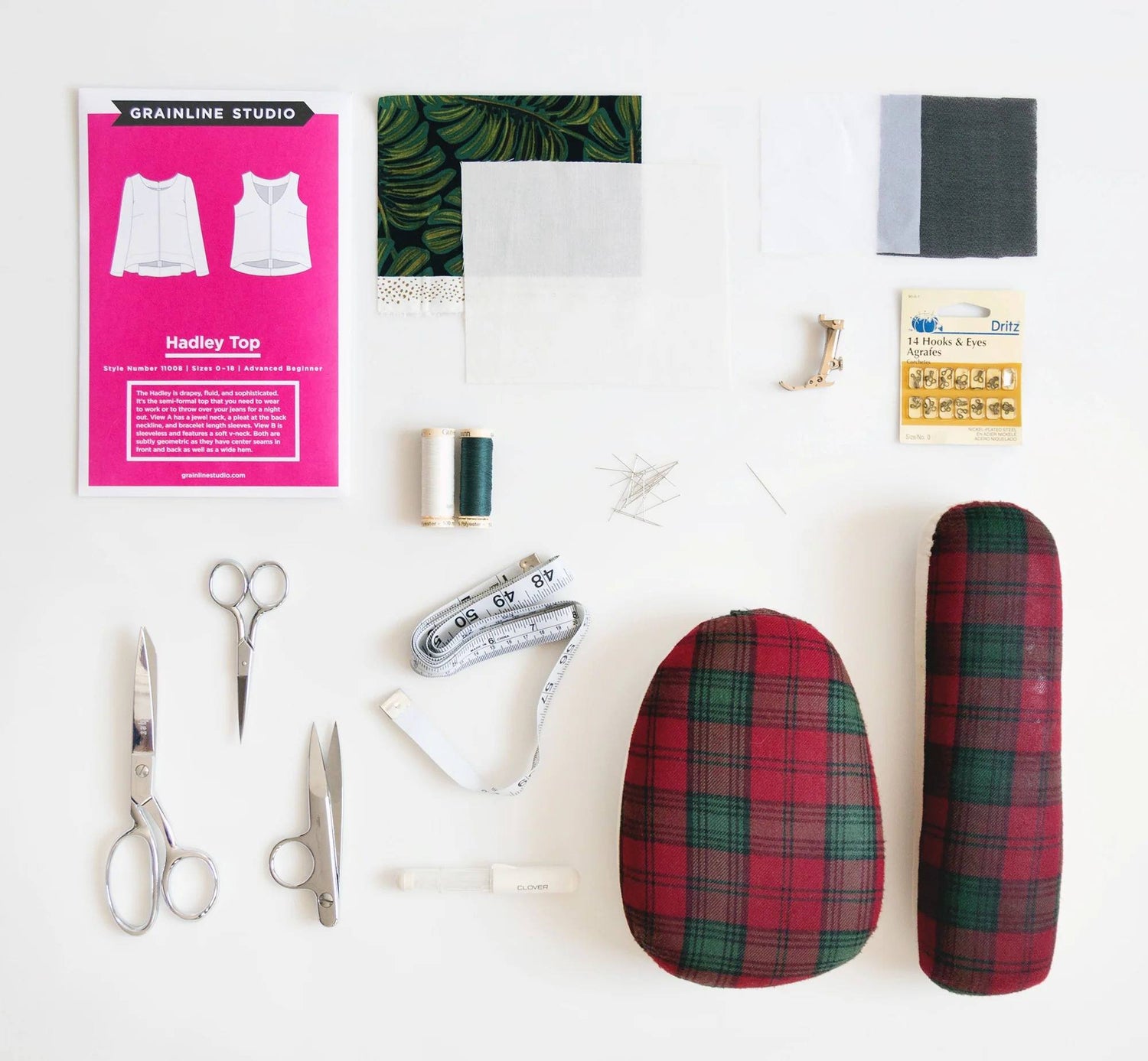 Flat lay of sewing supplies including Hadley pattern, fabric swatches, thread, scissors, measuring tape, hooks and eyes, and ham.