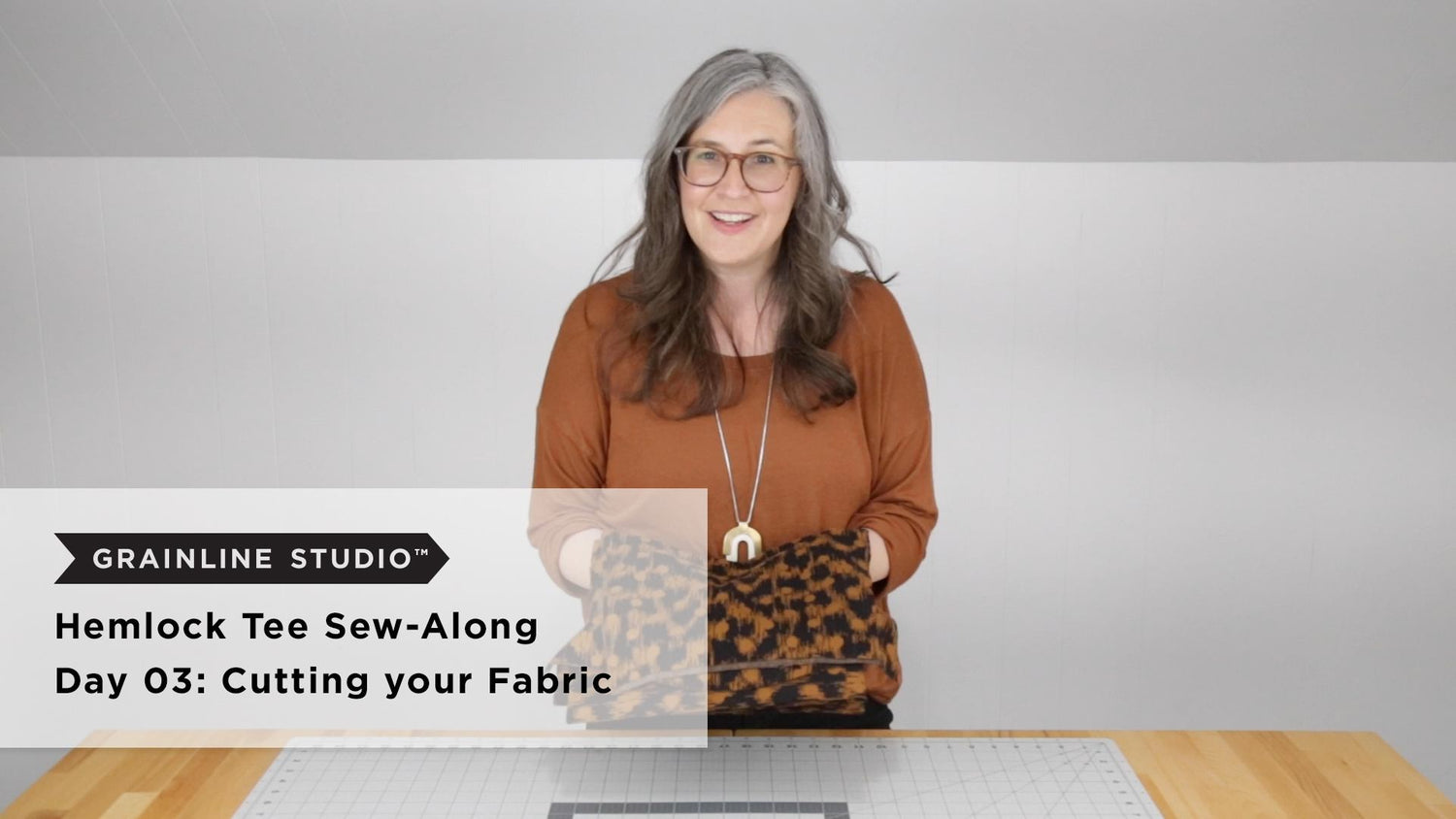 Hemlock Tee Sew-Along Day 03 thumbnail, woman holding folded wool knit fabric over cutting mat