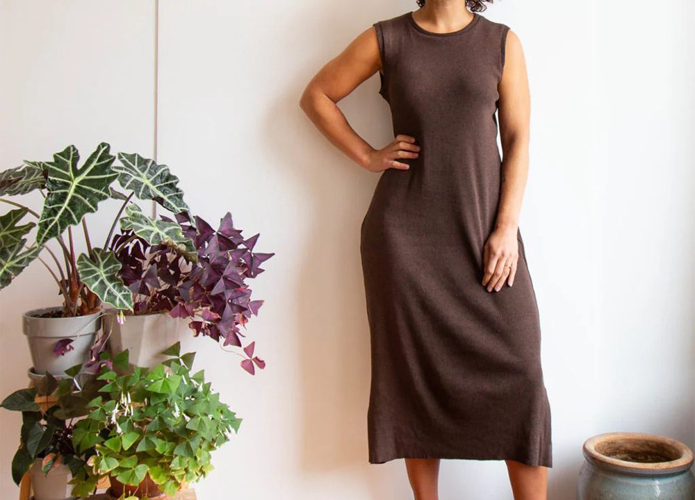 Brown sleeveless Lark Tee dress on model hitting mid-calf with relaxed slim fit and side slits, styled with plants