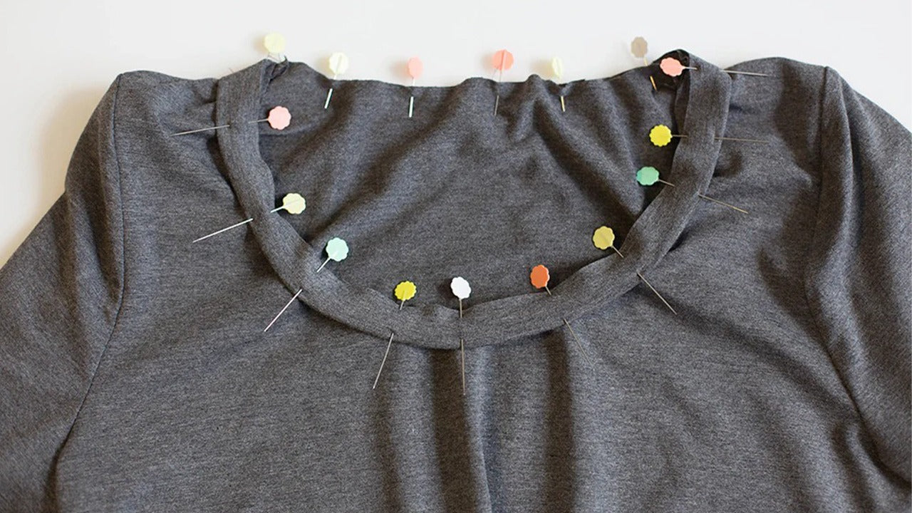 Gray Lark Tee neckline with folded neckband pinned at quarters showing colorful pins marking alignment points for sewing