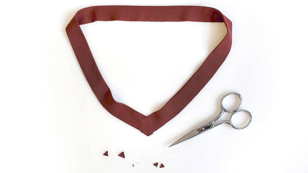 Brick red V-neck neckband folded and pressed with trimmed points beside scissors showing preparation for attaching to Lark Tee