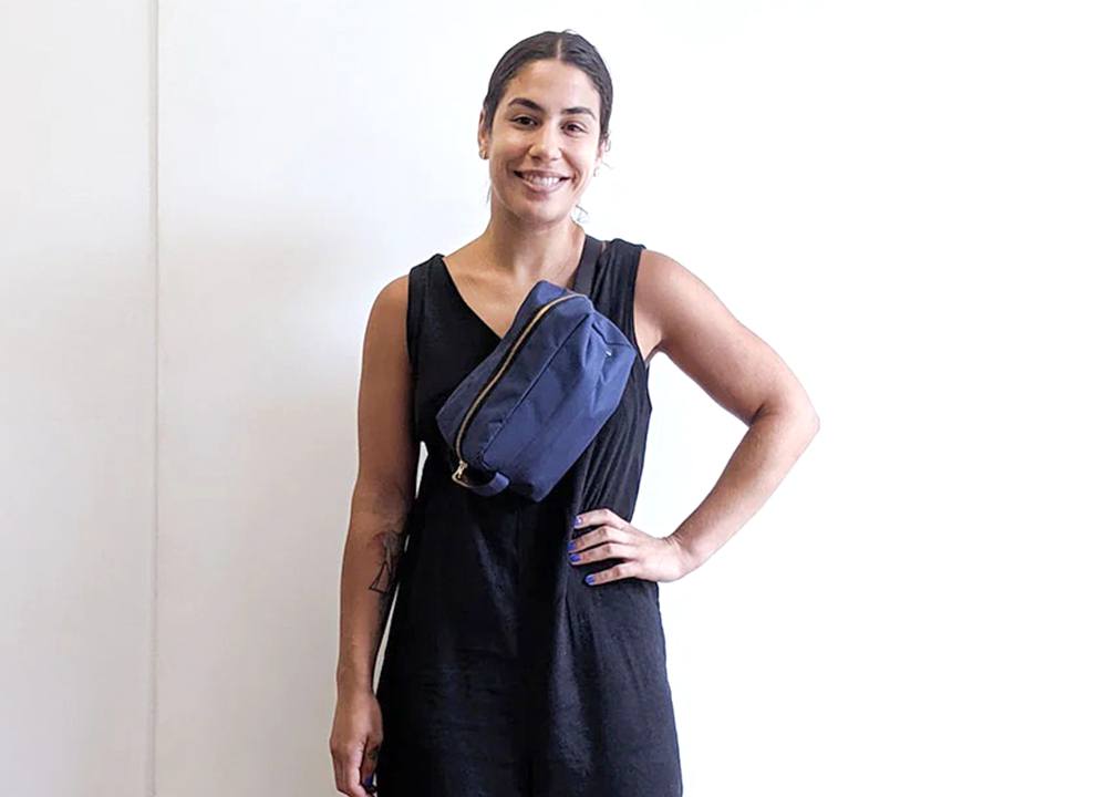 Woman wearing blue Portside dopp kit modified as crossbody fanny pack with black webbing strap over black sleeveless dress