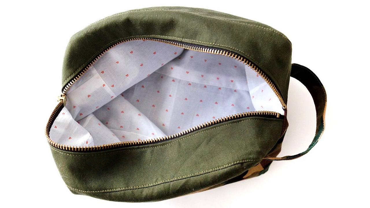 Dopp kit opened showing pink hearts lining hand-stitched inside olive green exterior with both zippers and front pocket visible