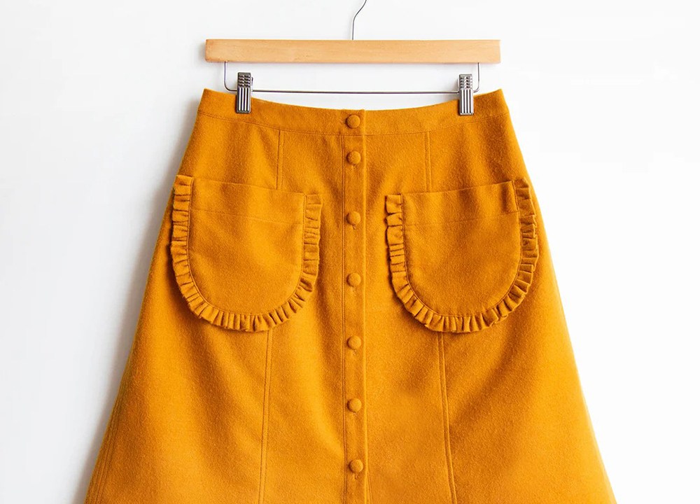 Reed Skirt in mustard yellow wool on hanger showing modified patch pockets with gathered ruffle trim detail