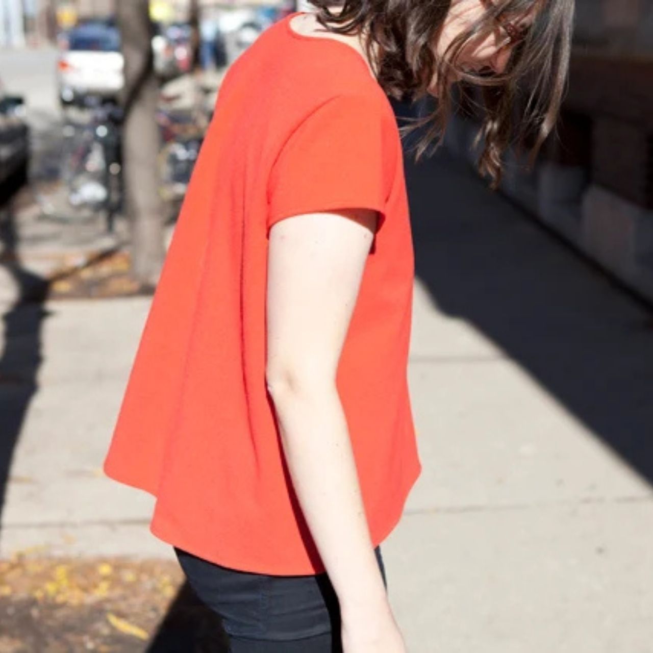 Side view of a Scout Tee with full back pattern hack in red wool, showing the flared swing silhouette on a city street.
