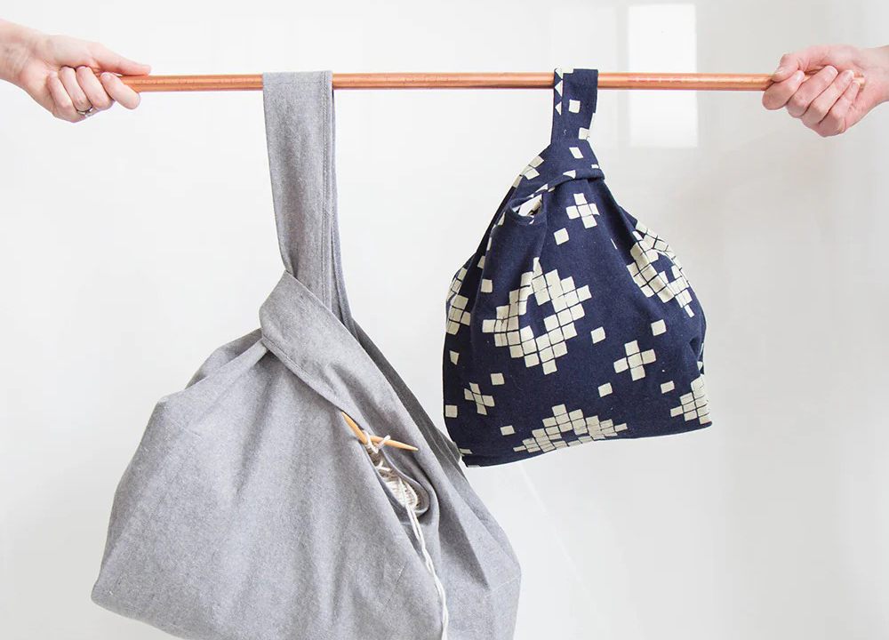 Two Stowe Bags hanging on wooden rod showing gray bag with permanent gusset and navy geometric bag without gusset
