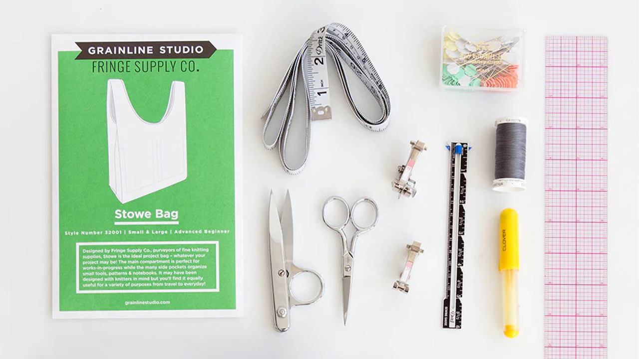 Stowe Bag pattern envelope with sewing supplies including measuring tape, scissors, rulers, thread, pins, and pink grid fabric