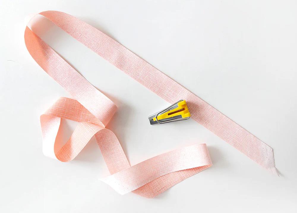 Pink bias tape strip with yellow bias tape maker tool ready for folding into double-fold binding