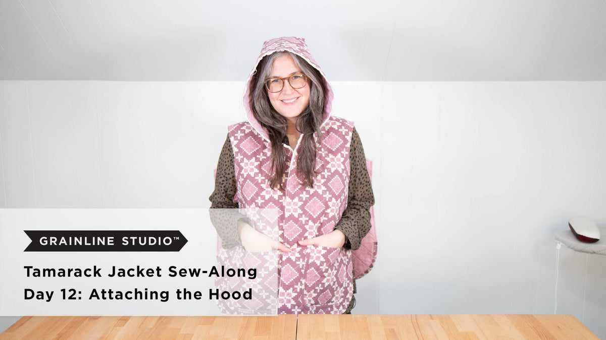 A smiling person wearing a sleeveless quilted Tamarack jacket in pink floral print with the hood up on a white background