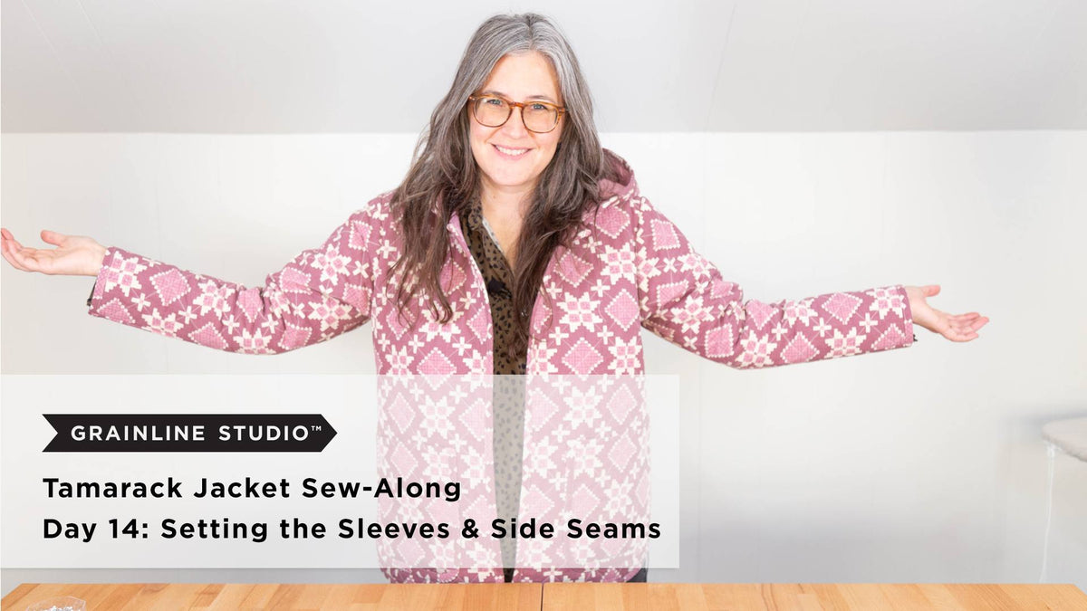 A smiling person wearing a completed quilted Tamarack jacket with hood in pink floral print with arms outstretched on a white background