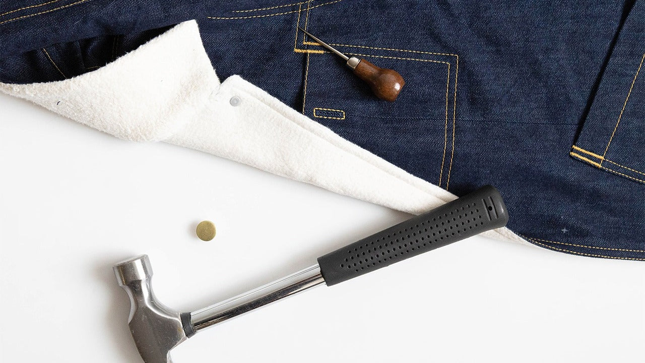 Thayer Jacket in navy denim with brass snap closure, hammer, and awl showing hardware installation for front closure finishing