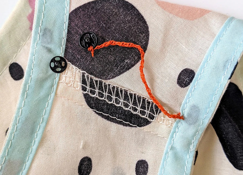 Hand forming thread chain loop and completed chain with snap attached to polka dot fabric armhole edge.