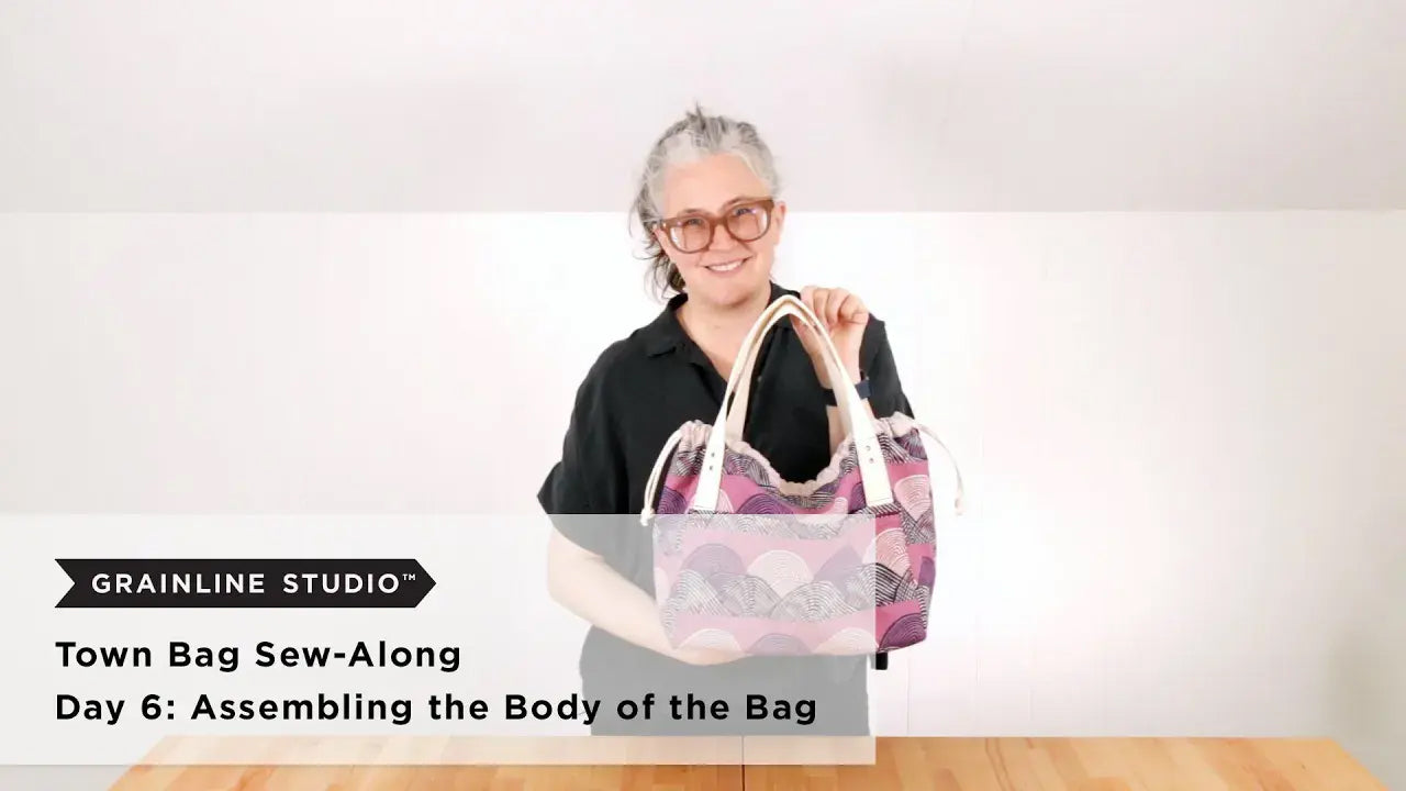 Woman holding a completed purple printed Town Bag with white cotton webbing handles and drawstring closure pulled closed.
