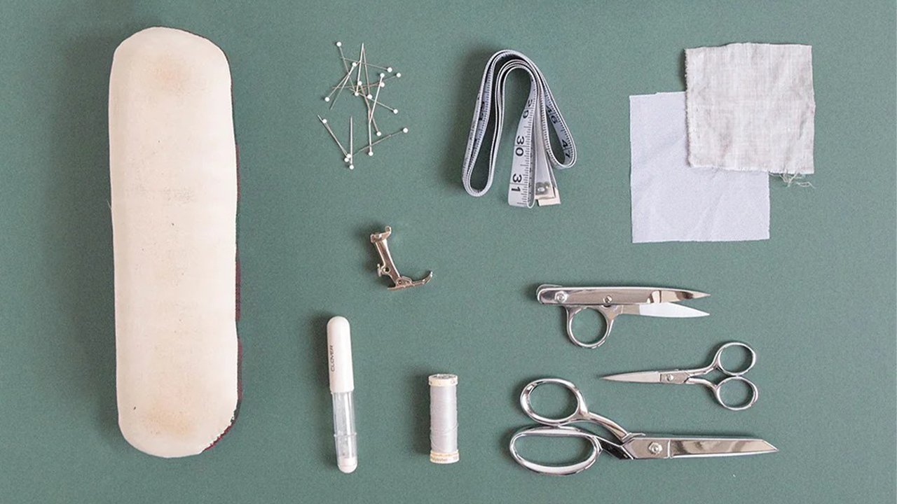 Sewing supplies for Uniform Tunic including ham, pins, tape measure, interfacing, marking pen, thread, and scissors on green