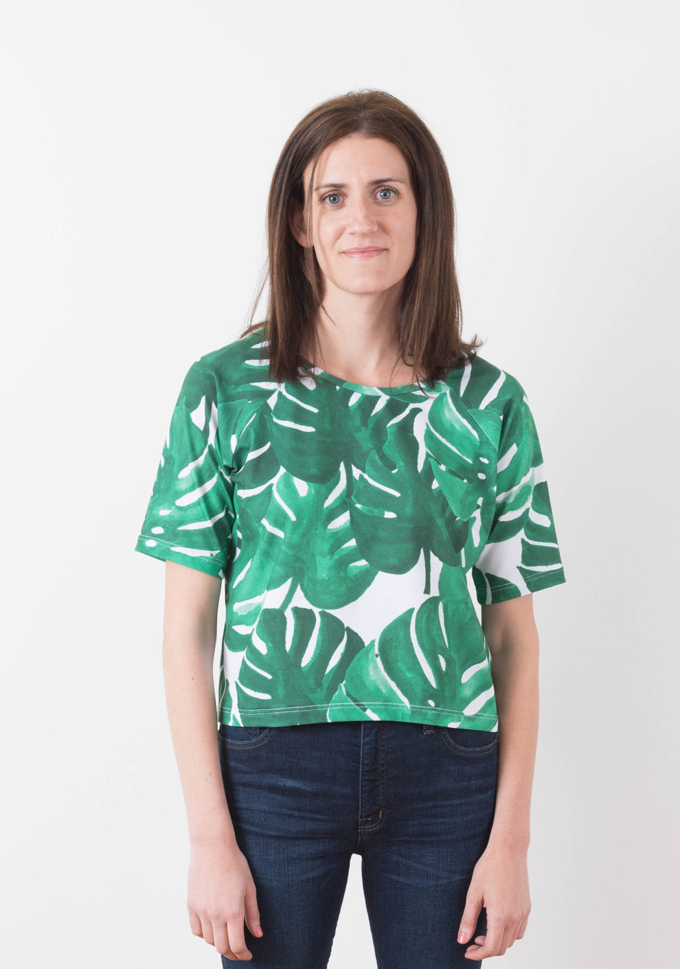 Front view of a woman wearing a short-sleeve Linden Sweatshirt in green monstera print knit fabric.