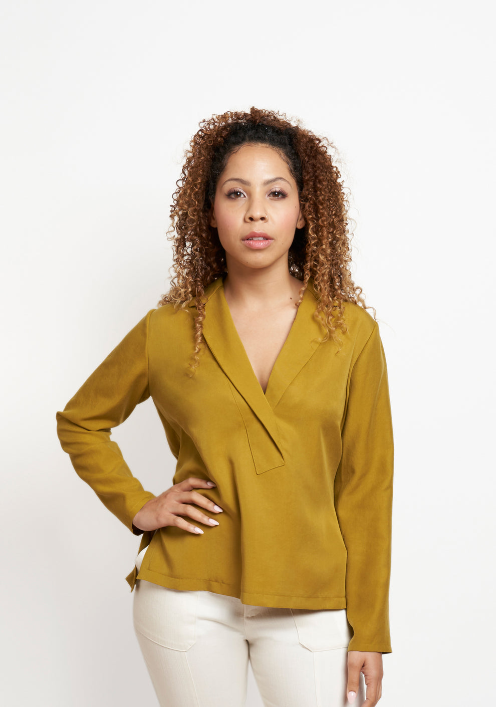 Front view of mustard Augusta Top with long sleeves, worn untucked and styled with white pants.