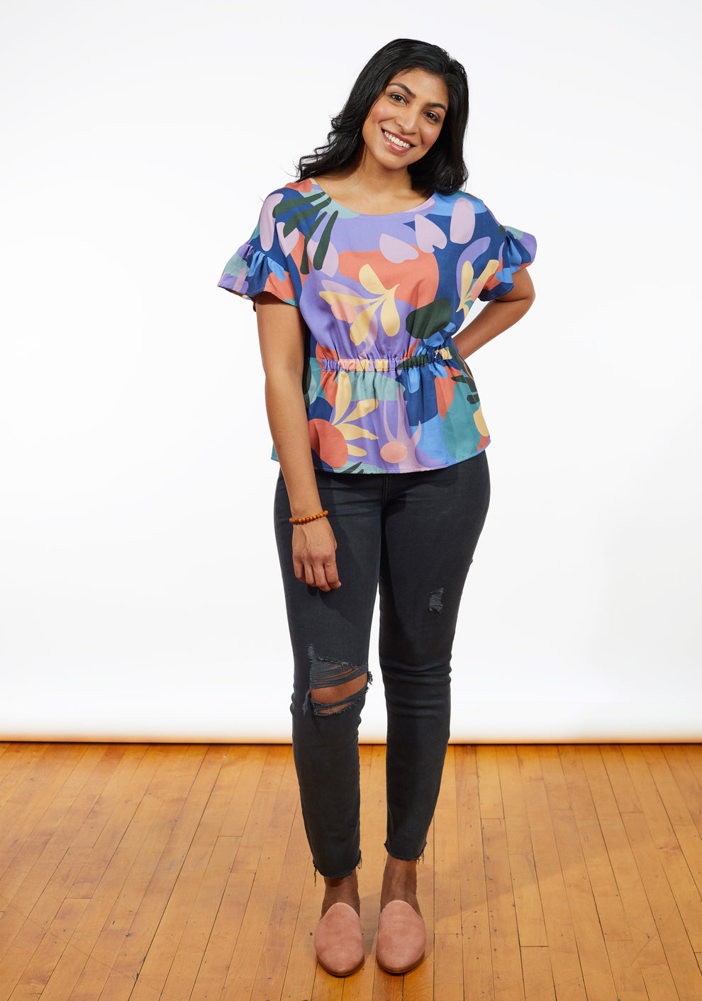 Playful front view of Corin Top with colorful print and gathered waist paired with ripped jeans.