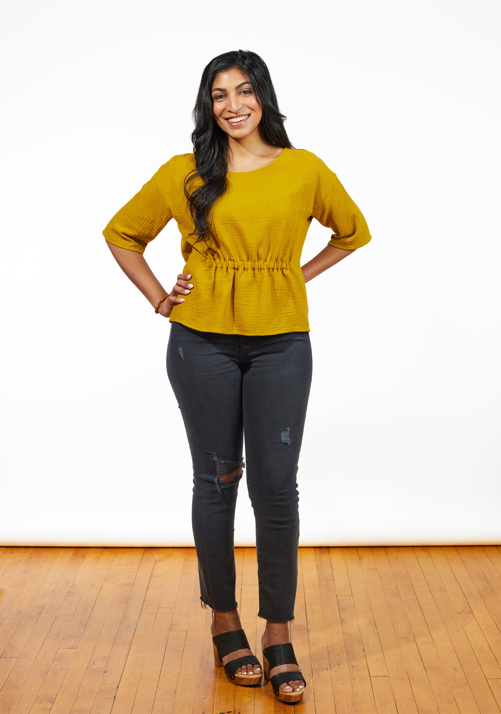 Model in mustard Corin Top with hands on hips wearing distressed jeans and platform shoes.