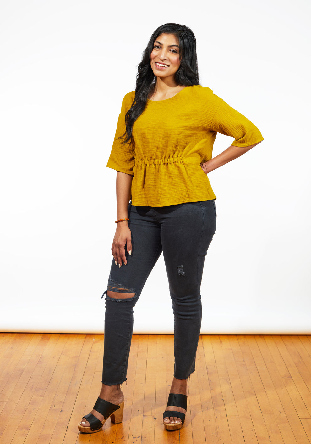 Model wearing mustard Corin Top standing with hand on hip and smiling.