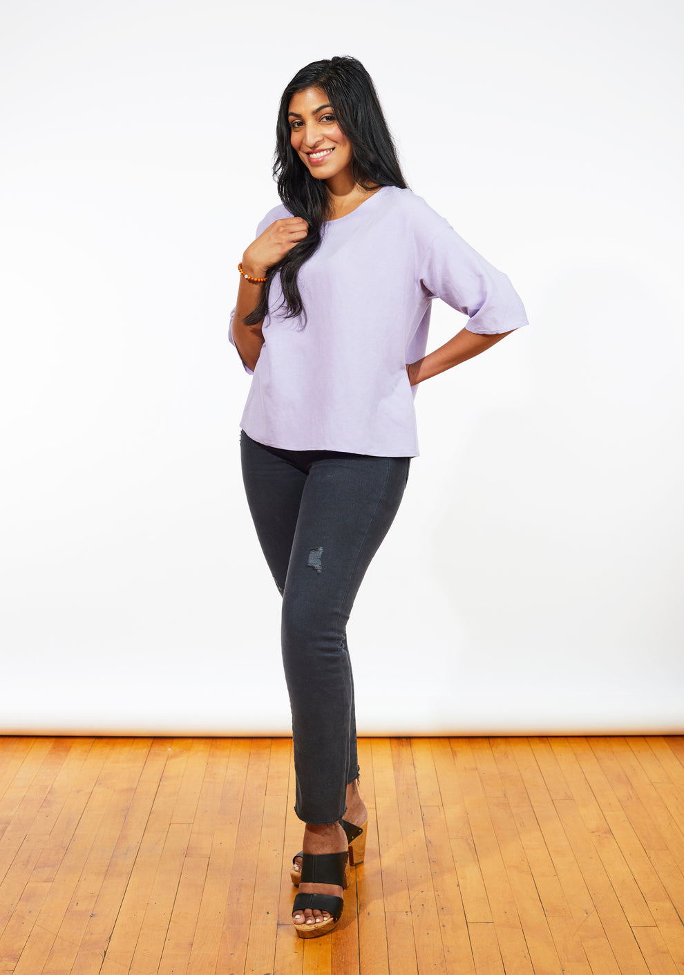 Model smiling in lilac Corin Top with relaxed fit, hand on hip, and elbow-length sleeves.