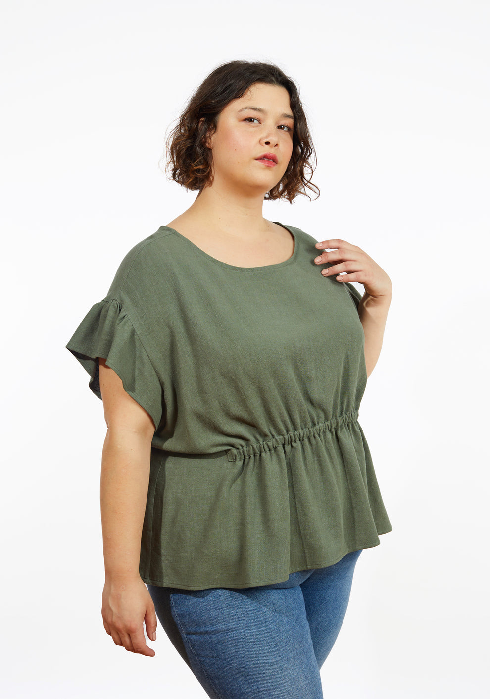 Three-quarter view of Corin Top with dropped shoulder flounce sleeves and gathered waist, shown in olive linen on model.