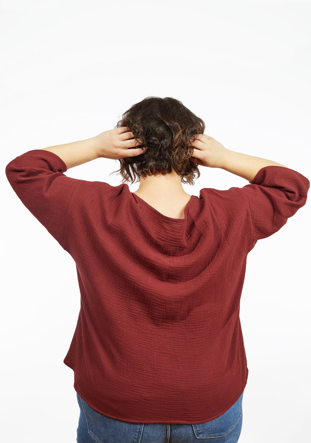 Model with hands at head wearing Corin Top in brick double gauze, showing back neckline and sleeve details.