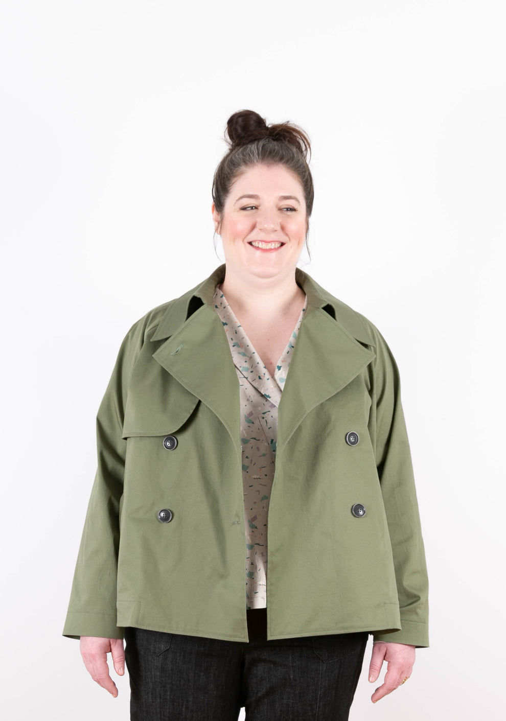 Model wearing green Cortland Trench open over printed blouse, smiling at camera.