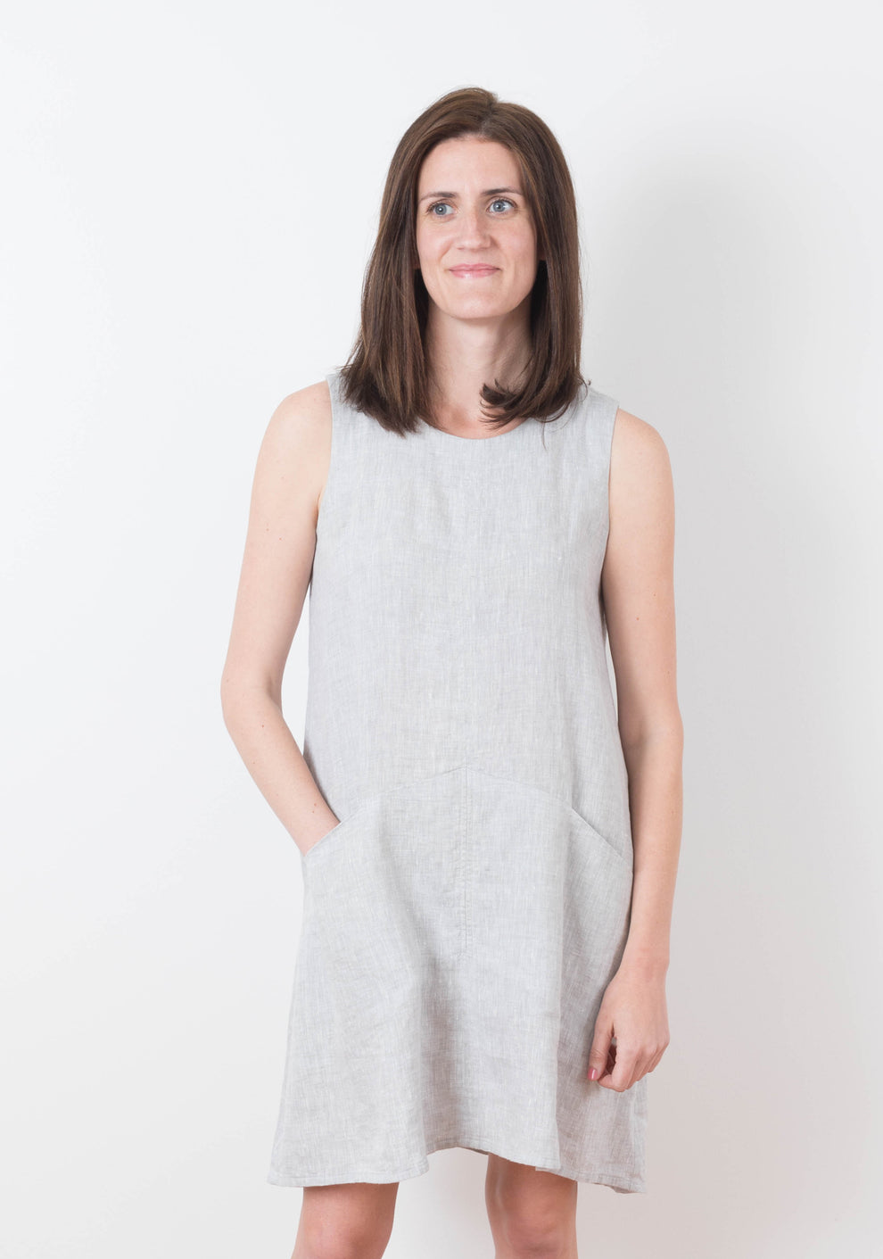 Model wearing sleeveless Farrow Dress in solid light grey fabric with front pockets, view A.