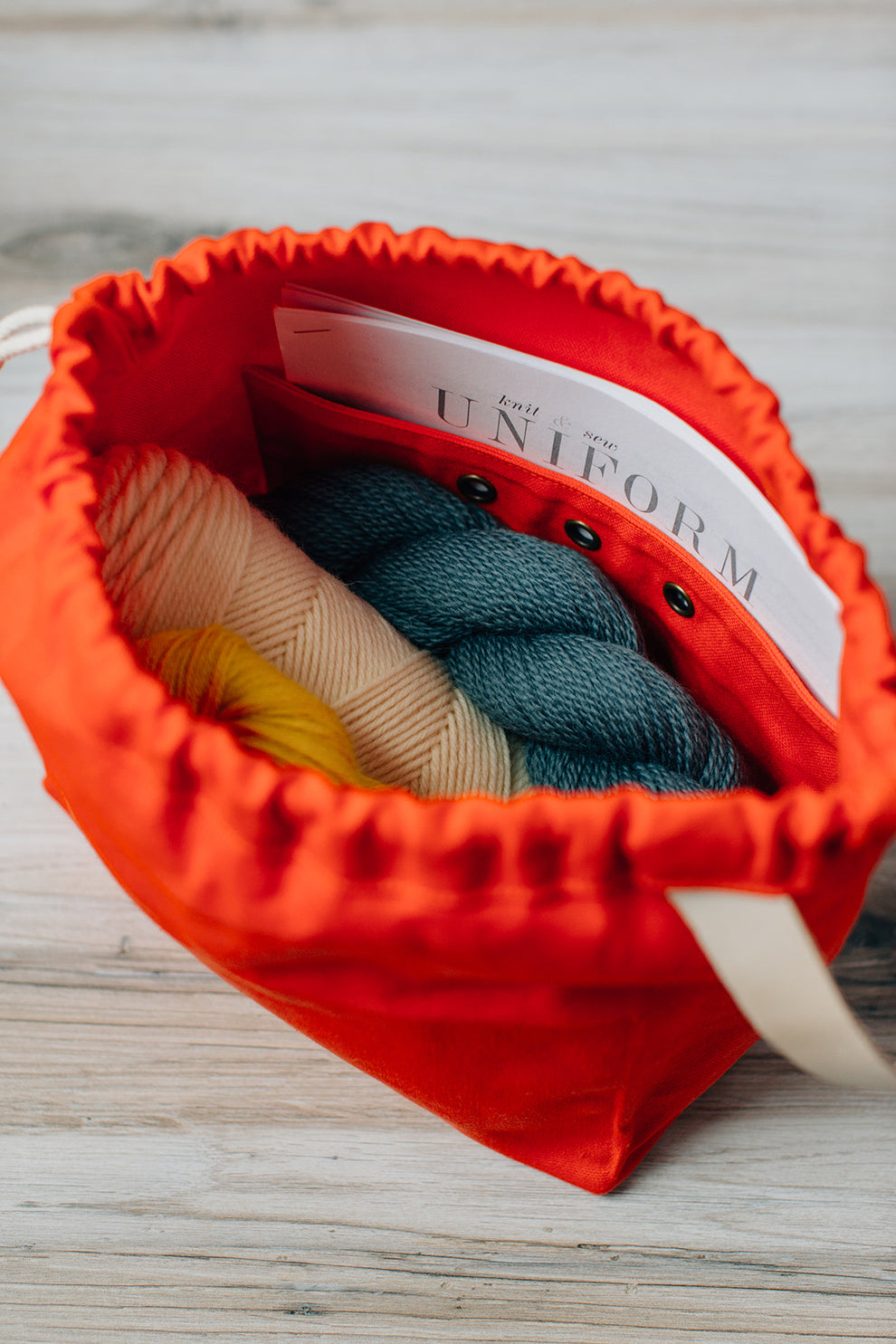 Close-up of orange field bag with yarn and pattern booklet visible inside.