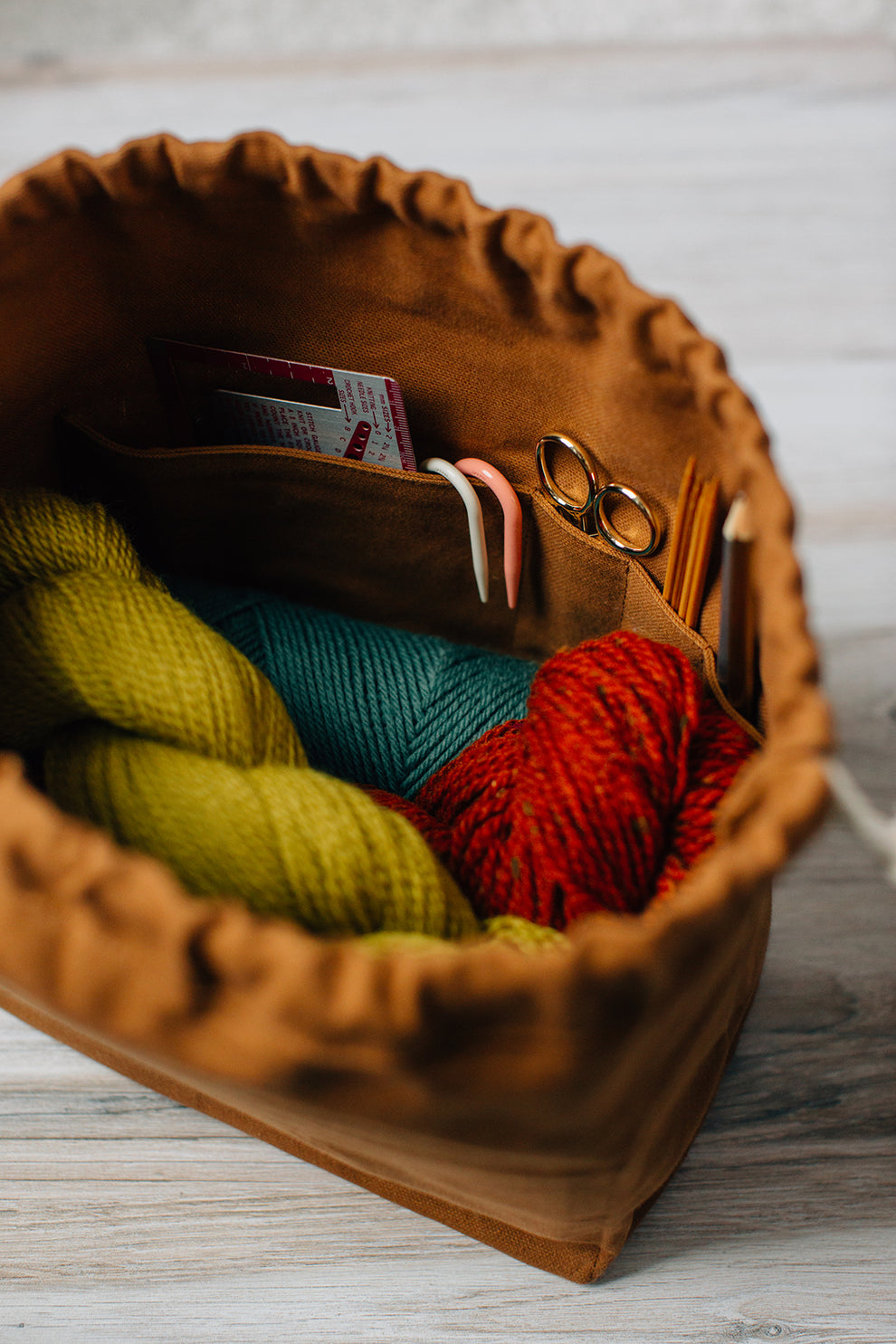 Interior of toffee field bag with colorful yarn and knitting tools inside pockets.
