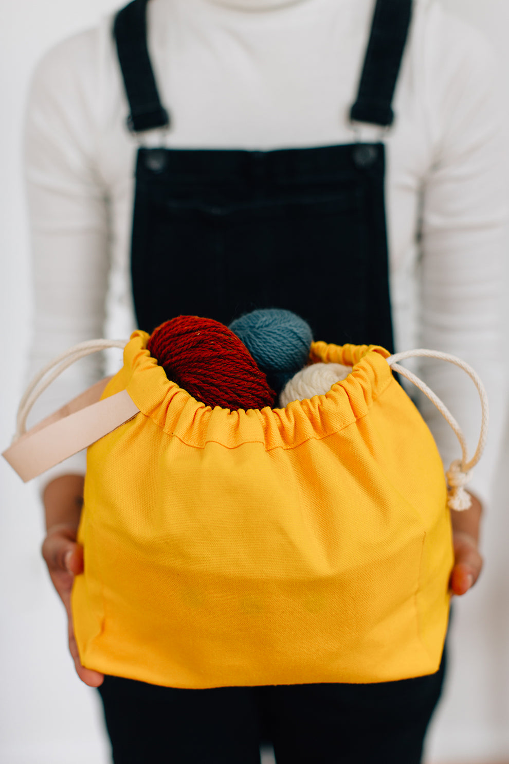 Person holding yellow field bag full of yarn in front of their torso with both hands.