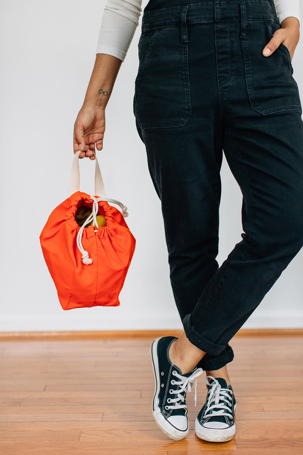 Person wearing black pants holding a bright orange field bag by the handle.