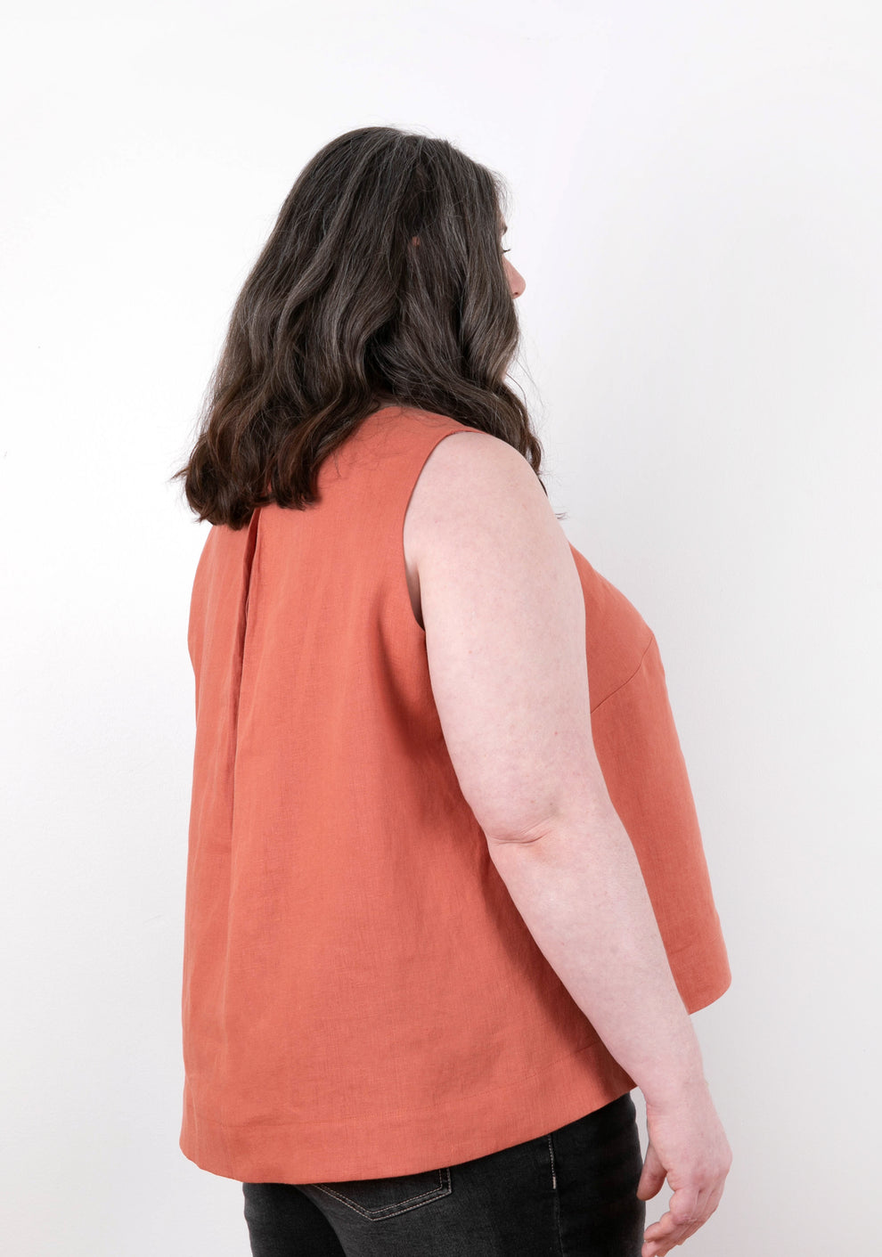 Back view of sleeveless coral Hadley Top on model, highlighting center back pleat and hemline.