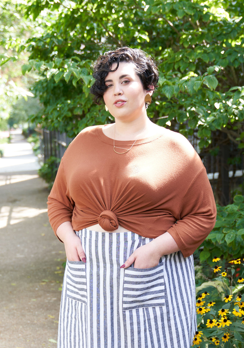 Model:Size 28, 5'7" | Outdoor view of model in Hemlock Tee tied at waist with long sleeves and striped skirt.