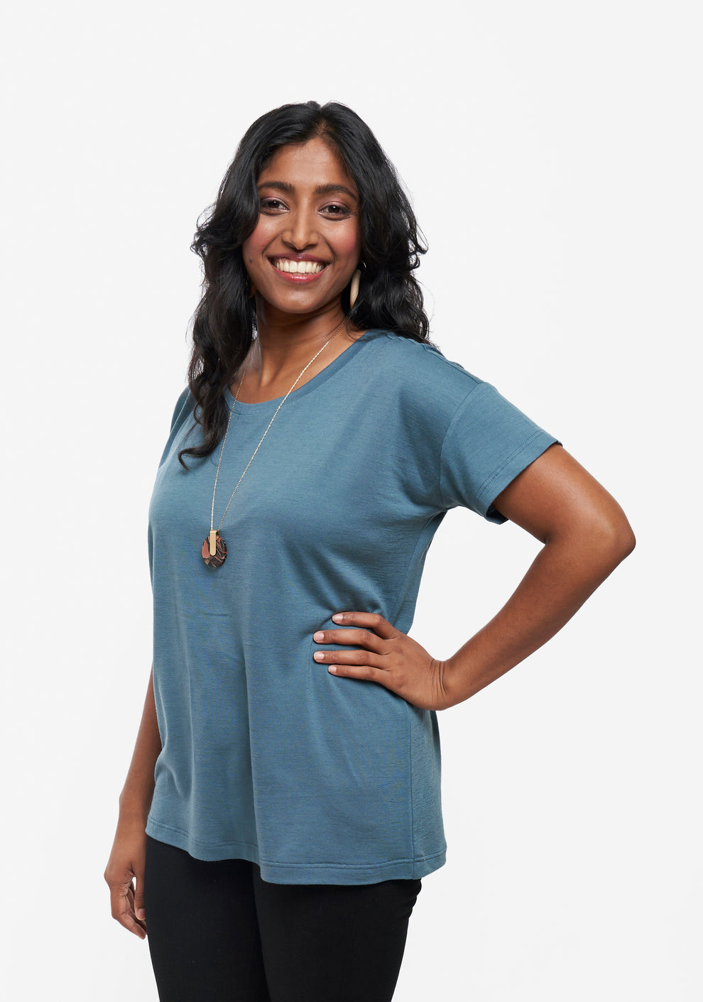Side view of model in hip length Hemlock Tee with short sleeves in teal, paired with pants.