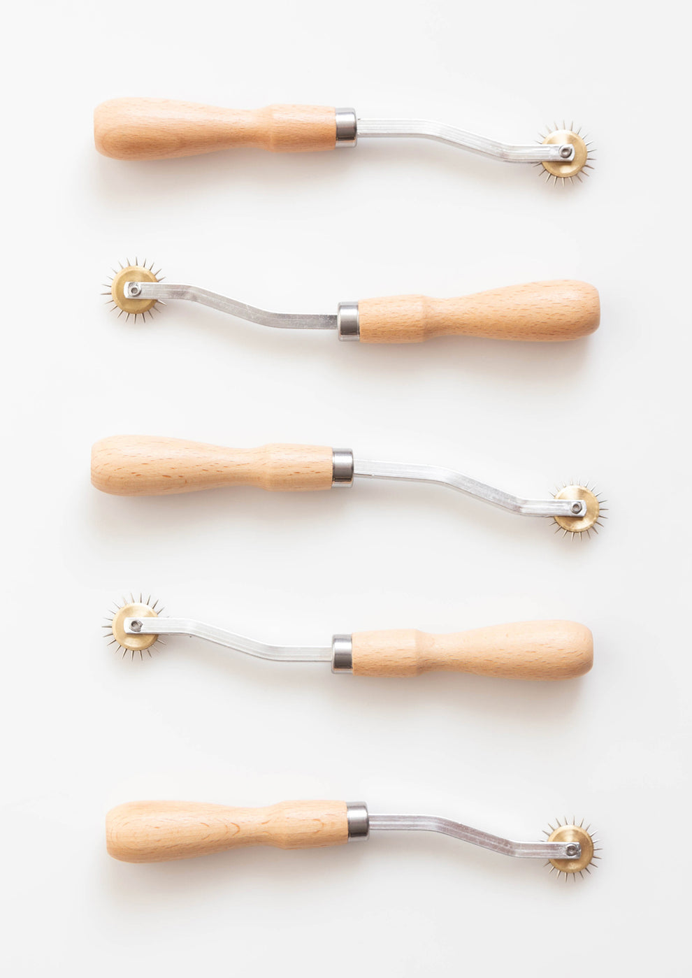 Flatlay of five tracing wheels with wood handles and spiked wheels on white background.