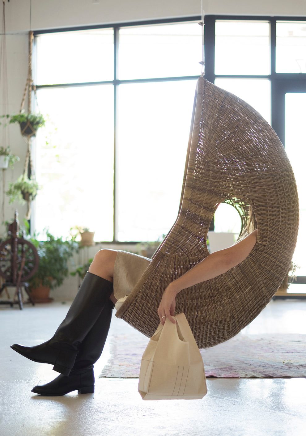 Person lounging in a wicker chair and holding a small cream-colored Stowe Bag.