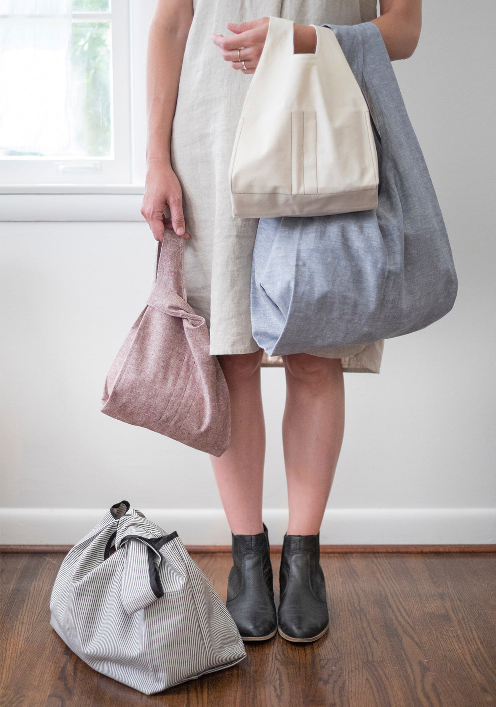 Person holding four sizes of handmade Stowe Bags in various colors while standing indoors.