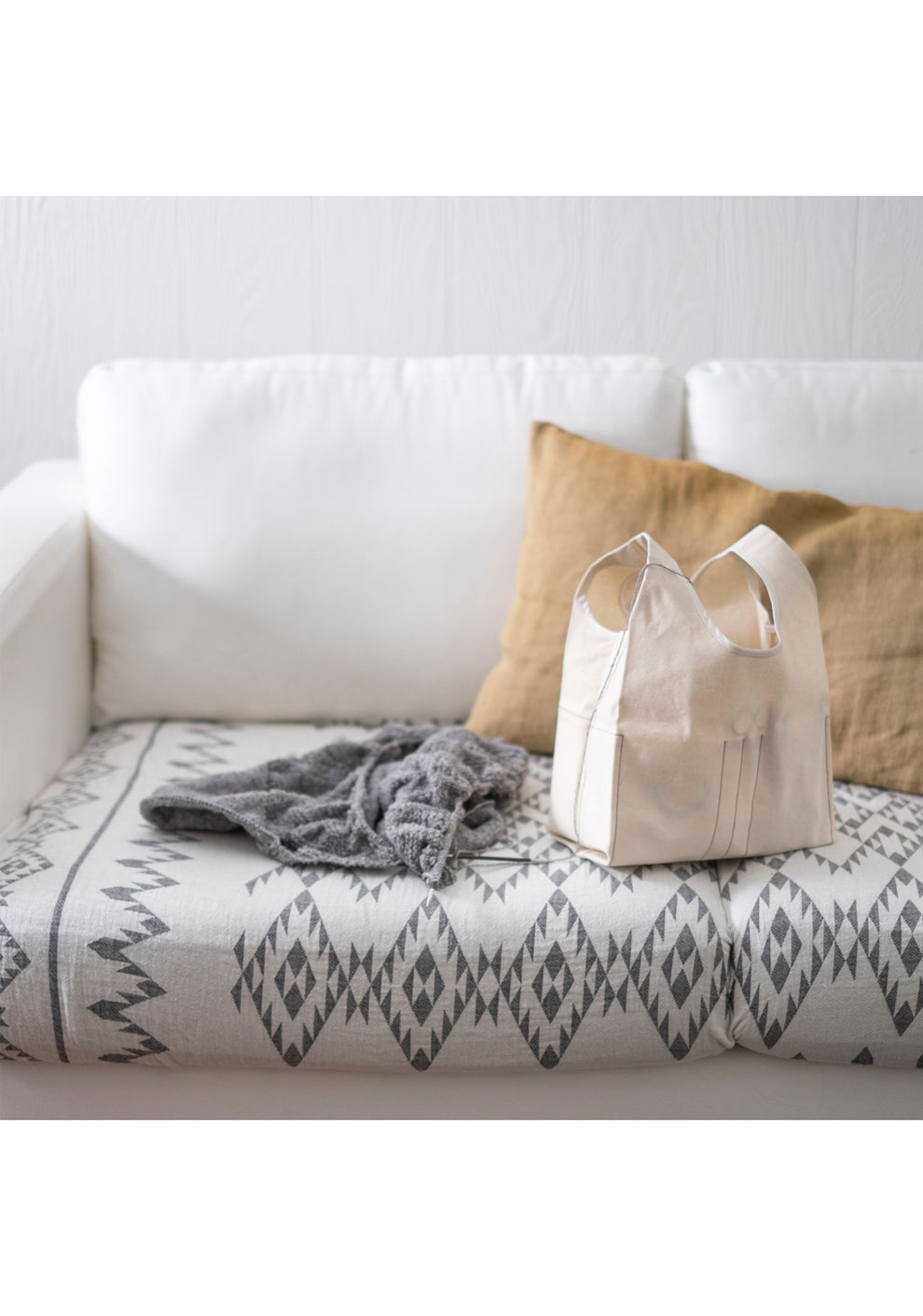Cream Stowe Bag and gray knitting project resting on a patterned sofa with pillows.