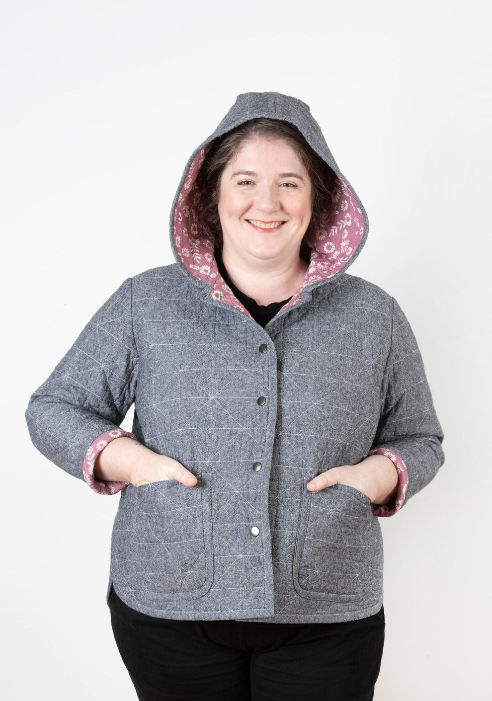 Front view of model smiling in gray Tamarack Jacket with hood up and pink floral lining.
