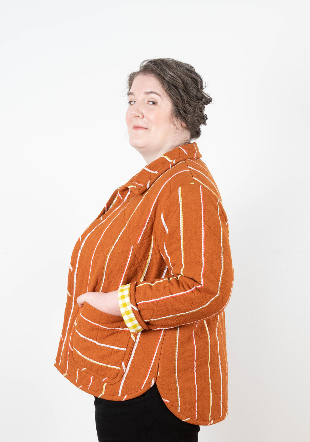 Side view of orange striped Tamarack Jacket with collar add-on and visible yellow gingham lining.