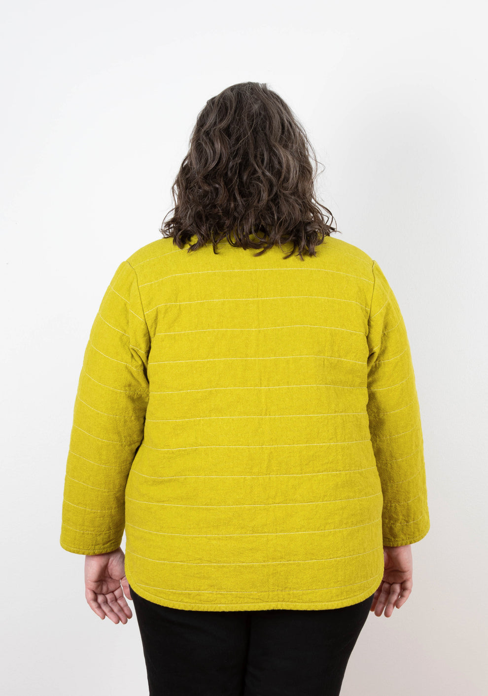Back view of Tamarack Jacket in mustard yellow linen, showing horizontal quilting lines and relaxed fit.