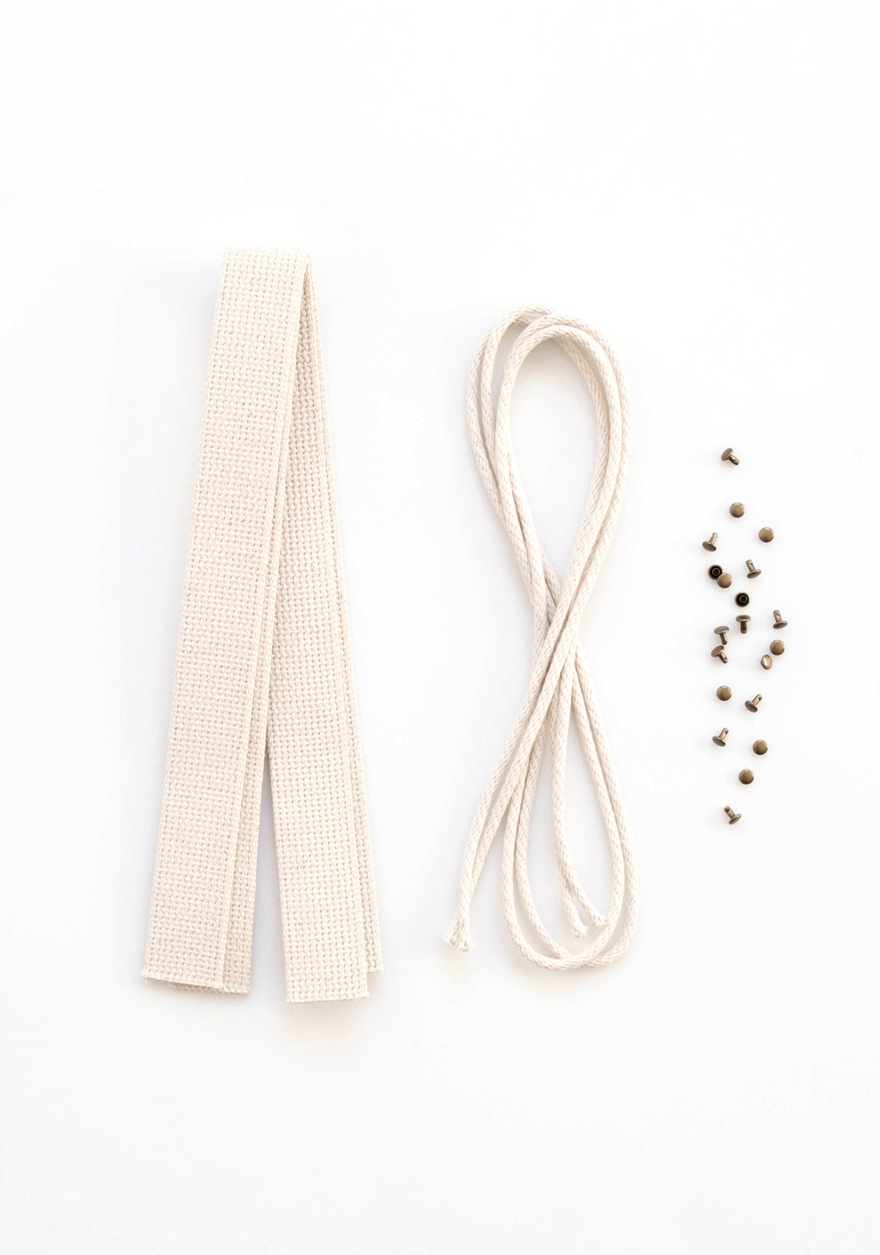 Flatlay of Town Bag Notions Kit showing cotton webbing handles, drawstring cord, and antique brass rivets on white background.