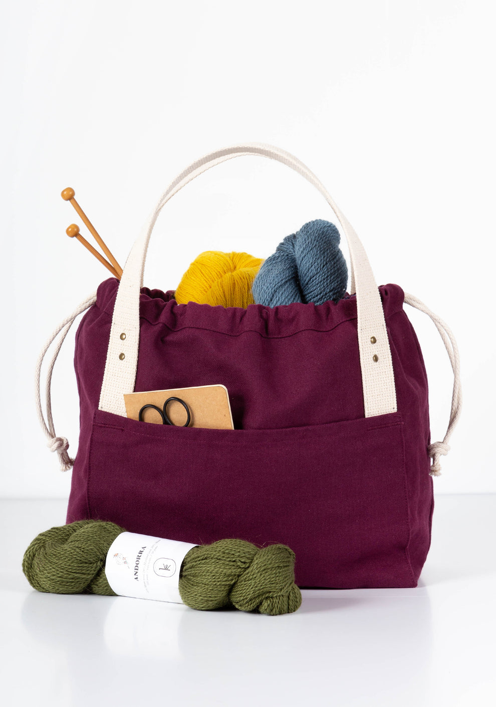 Plum canvas Town Bag filled with yarn and tools, front view with handles upright.